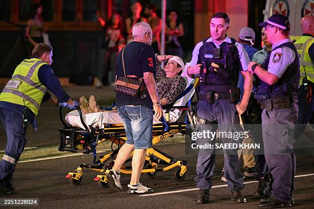 Health workers move a woman on a stretcher to an ambulance after a shooting incident at Bondi Beach in Sydney on December 14, 2025. Australian police...
