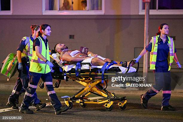 Health workers move a man on a stretcher to an ambulance after a shooting incident at Bondi Beach in Sydney on December 14, 2025. Australian police...