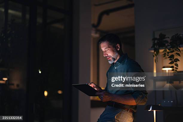 quiet night office scene with man using tablet, focused work at desk - warm light stock pictures, royalty-free photos & images