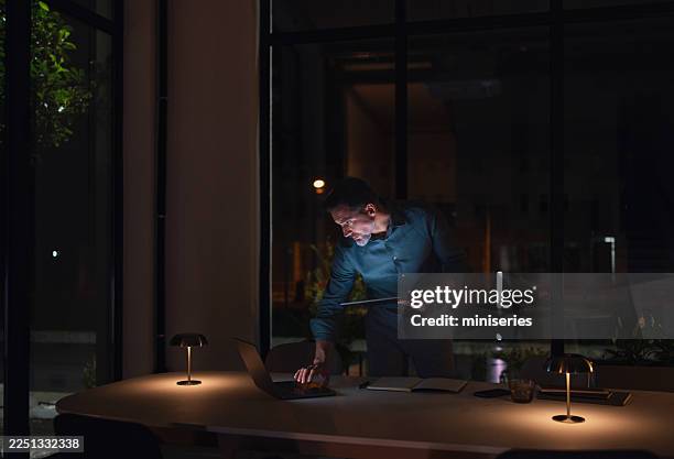 focused businessman working late at night in modern office with laptop and tablet - low lighting stock pictures, royalty-free photos & images