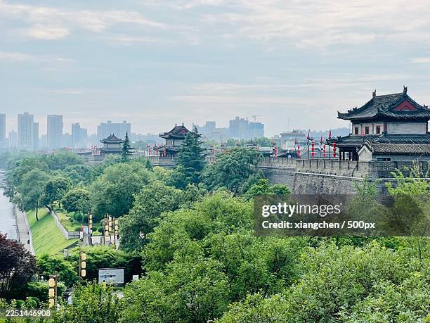 ancient city wall and traditional buildings of xian, china, with modern skyline in the background, surrounded by lush green trees - fortified wall stock pictures, royalty-free photos & images