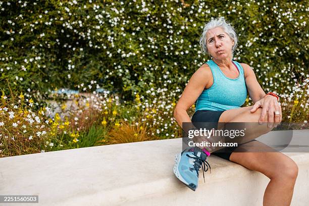mature woman injuring her ankle while jogging in a public park in barcelona in spain - twisted ankle stock pictures, royalty-free photos & images