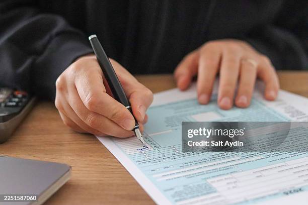 close-up views of hands organizing tax forms and financial documents at a home workspace with calculator, laptop and pen, natural light highlighting the detailed process of tax preparation and personal finance management for business and editorial use - tax time stock pictures, royalty-free photos & images