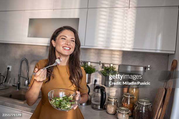 woman enjoying healthy salad in modern kitchen - green salad stock pictures, royalty-free photos & images