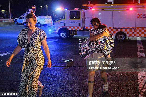 Member of the public leaves the scene with her child, who is covered in an emergency blanket, after a shooting at Bondi Beach on December 14, 2025 in...