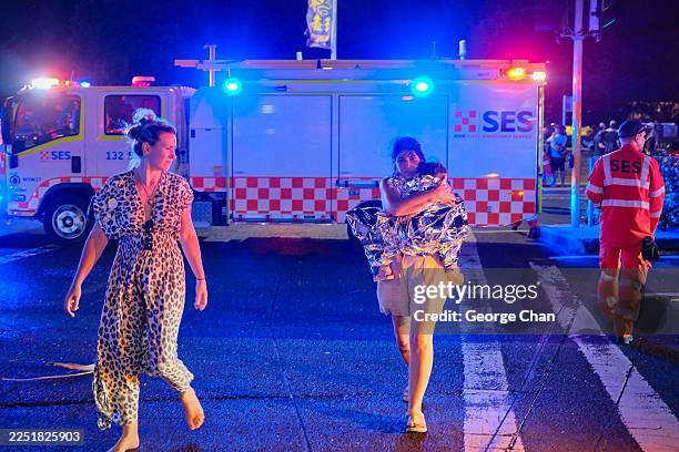 Member of the public leaves the scene with her child, who is covered in an emergency blanket, after a shooting at Bondi Beach on December 14, 2025 in...