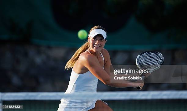young female tennisplayer hitting a backhand by the net - tennis player stock pictures, royalty-free photos & images