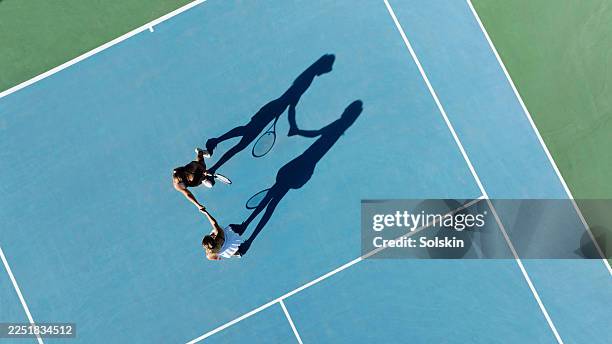 two young female tennis player shaking hands over tennis net after match - fairness stock-fotos und bilder