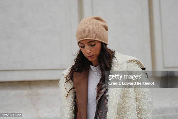 Gabriella Berdugo wears long dark brown hair styled in loose waves under a beige knit beanie hat, natural makeup with defined brows, neutral lips,...