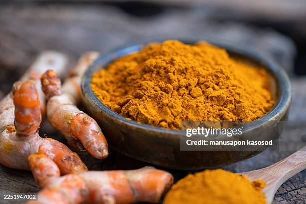 turmeric powder and fresh turmeric in wood bowls on wooden table. - curcuma photos et images de collection
