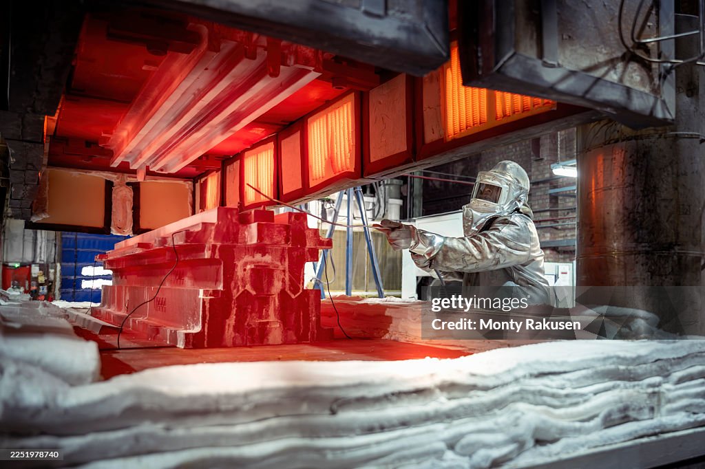 Engineer in heat protective suit operating high temperature titanium press in aerospace parts factory