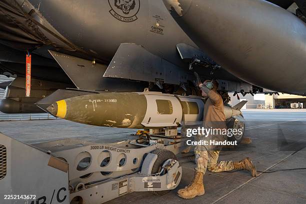 In this handout photo in an undisclosed location, a U.S. Airman attaches a GBU-31 munitions system to an F-15E Strike Eagle in the U.S. Central...