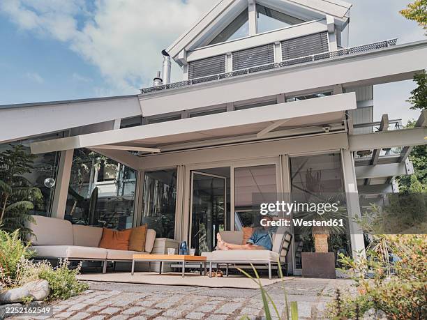 man relaxing on patio with lounge furniture at modern villa in summer - awning stock pictures, royalty-free photos & images