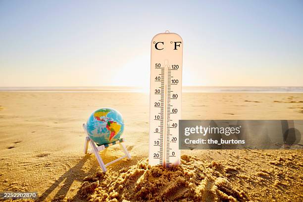 thermometer in sandcastle and small deck chair with globe at beach against sun - ola de calor fotografías e imágenes de stock