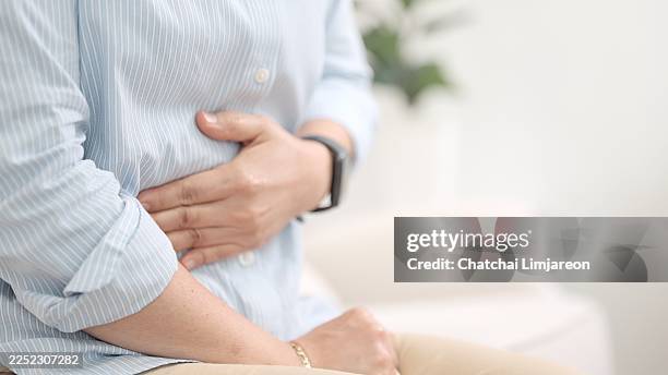 primo piano. la donna si stringe forte lo stomaco con entrambe le mani, mostrando il volto dolorante dovuto a dolori addominali e crampi, probabilmente dovuti a un disturbo digestivo o a un problema di salute cronico. supporto sanitario per una popolazione - apparato digerente umano foto e immagini stock