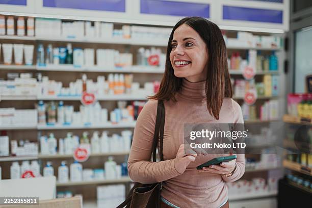 woman smiling and using phone in pharmacy - satisfaction stock pictures, royalty-free photos & images