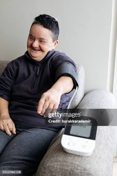 senior woman with down syndrome measuring blood pressure - developmental disability stock pictures, royalty-free photos & images