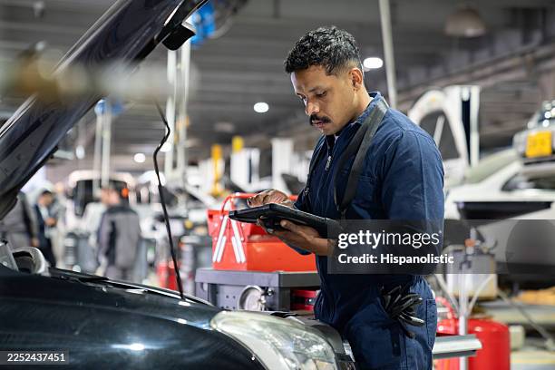 mechanic using a digital tablet while making a diagnosis on a broken car - auto mechanic stock pictures, royalty-free photos & images