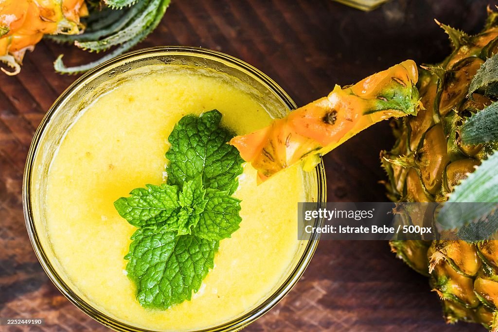 Refreshing pineapple smoothie or juice garnished with fresh mint, served on a rustic wooden table with a whole pineapple