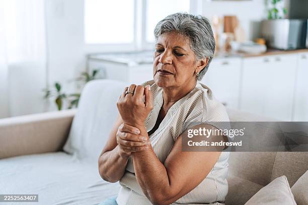 senior woman touching painful wrist at home - inflamação imagens e fotografias de stock