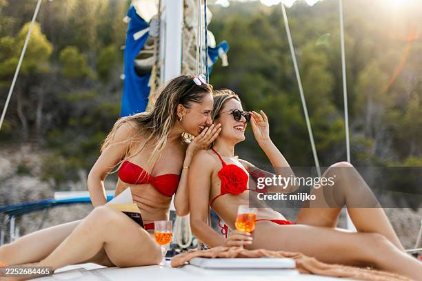 two women sitting on a sailboat's deck drinking wine and having a relaxing time - recreational boat stock pictures, royalty-free photos & images