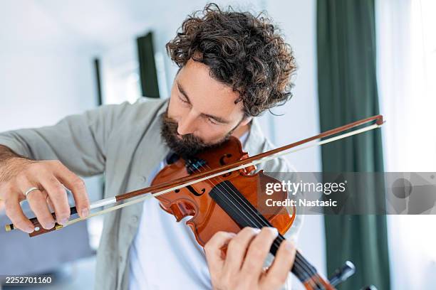 male musician playing violin in warm home interior - classical musician stock pictures, royalty-free photos & images