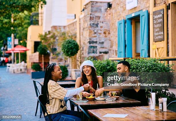 joyful friends enjoying drinks and food together at an outdoor cafe table on a sunny city street - plano geral imagens e fotografias de stock