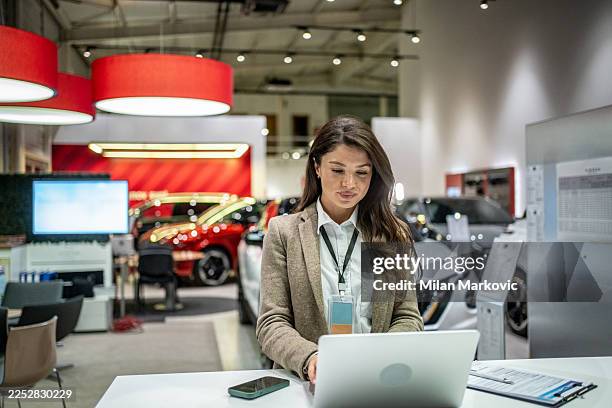 saleswoman using laptop working at car dealership showroom - sales executive stock pictures, royalty-free photos & images
