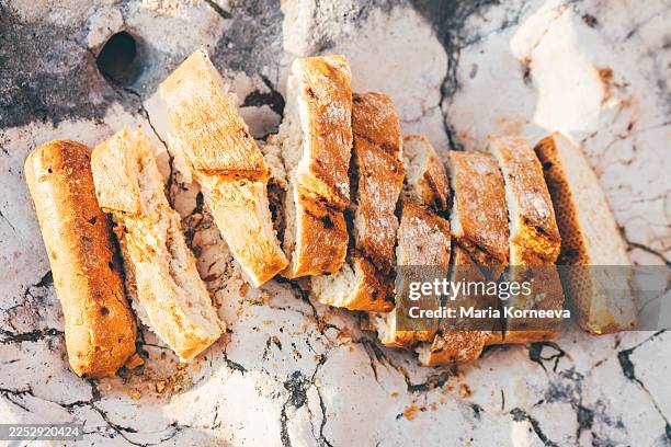 freshly sliced baguette pieces resting on a textured, sunlit stone surface outdoors. this rustic culinary composition evokes a sense of organic living, simple pleasures, and mediterranean-style dining. - garlic bread stock pictures, royalty-free photos & images