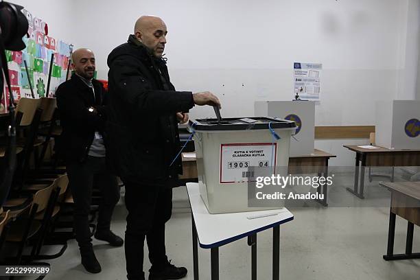 Man casts his ballot into a sealed ballot box as voting begins at a polling station during early general elections in Kosovo, marking the start of...
