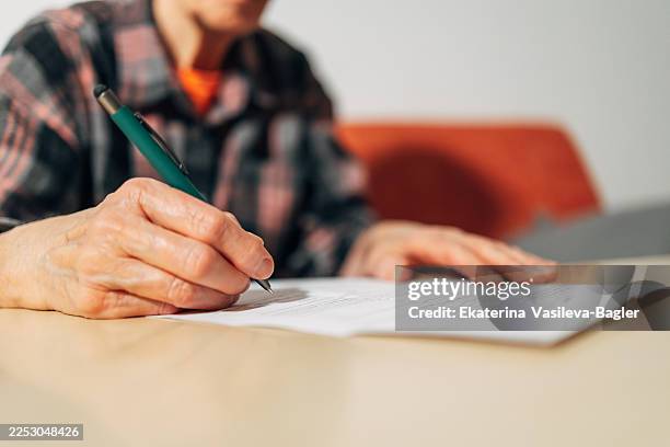 senior adult woman signing important legal document - testament photos et images de collection