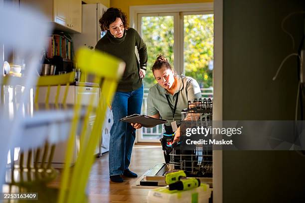 professional repairwoman explaining dishwasher problems to female houseowner in kitchen - house call stock pictures, royalty-free photos & images