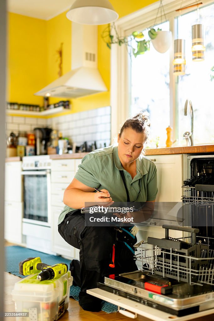 Female technician writing damaged products of dishwasher while working during house call service