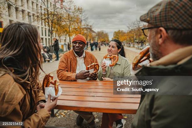 junges paar genießt ein date mit freunden in berlin, während sie brezeln in einer lebhaften außenatmosphäre teilen - breze stock-fotos und bilder