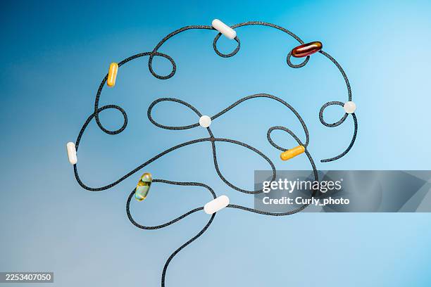 a conceptual representation of a human brain formed by a black wire with various colorful medicinal capsules attached. - drug abuse stock pictures, royalty-free photos & images