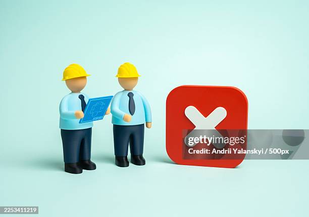 two miniature construction workers reviewing blueprints next to a large red x symbol, representing a problem or rejection - construction mistake stock pictures, royalty-free photos & images