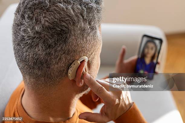 man using hearing aid during online video consultation at home - deaf signing stock pictures, royalty-free photos & images