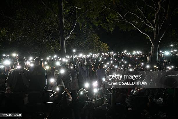 People turn on their mobile phones' flashlights as they observe a minute's silence to reflect on the tragic Bondi Beach shooting attack before New...