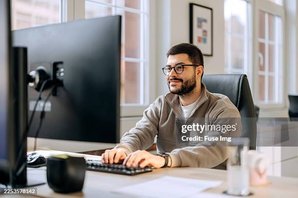 hombre vestido casualmente trabajando en una pc en la oficina - web designer fotografías e imágenes de stock