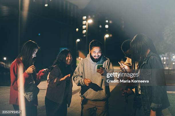 a group of young friends stands together at night, illuminated by the bright glow of their smartphone screens. - subculture stock pictures, royalty-free photos & images