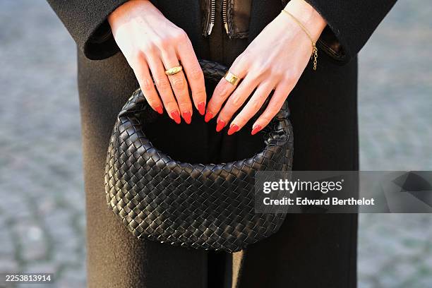 Amanda Derhy wears a golden ring, red nail polish, a black winter coat, a black woven leather bag by Anthropologie, during a street style fashion...