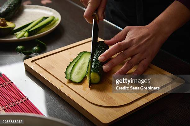 una persona affetta il cetriolo su un tagliere di legno in cucina, verdure fresche pronte per la cottura - pasta al pomodoro foto e immagini stock