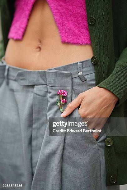 Alicia Aylies wears a gray high-waisted tailored trouser with a structured waistband and front pleats, styled with a gold-tone floral brooch...