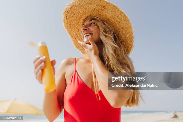 smiling woman applying sunscreen at the beach - sun radiation stock pictures, royalty-free photos & images