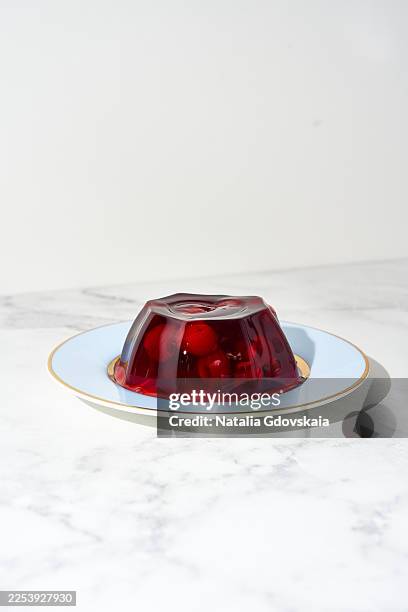 molded red gelatin with cherries served on a light blue plate with a gold rim. classic dessert on a marble countertop. new nostalgia - gelatin stock pictures, royalty-free photos & images