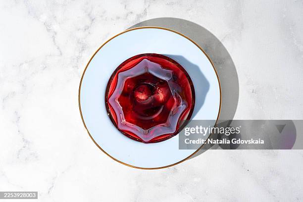 gourmet red gelatin dessert in a flower mold on a blue plate with a gold rim. top-down view of a single portion on a white surface with copy space. - gelatin stock pictures, royalty-free photos & images