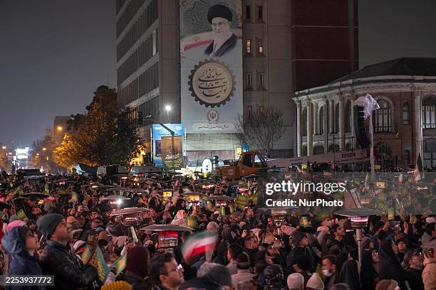 Iranian people wave the country's flags under a portrait of Iran's Supreme Leader, Ayatollah Ali Khamenei, during an unveiling ceremony of a statue...