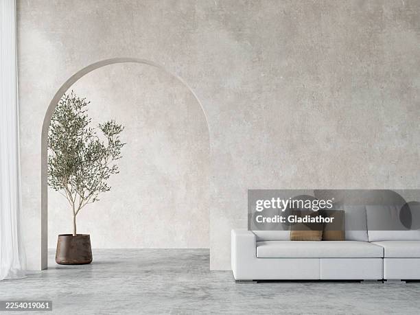 modern minimalist dining room with a white leather sofa in foreground, a potted olive tree in an arched niche in the cement textured wall in the background, window with curtains - simple living stock pictures, royalty-free photos & images