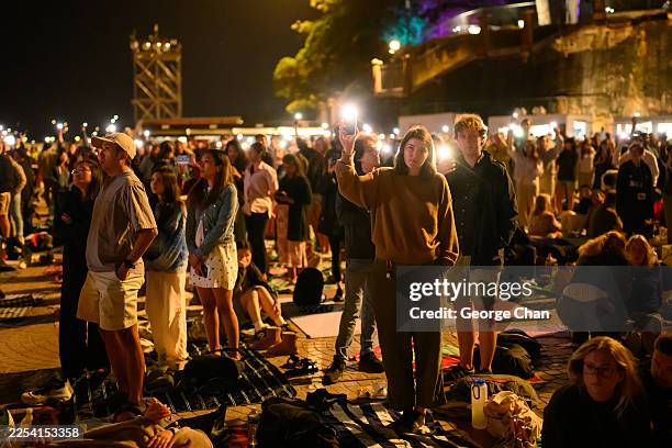 People at Opera House turn on the flashlight on their phone as they observe a minute of silence in honour of the victims of Bondi mass shooting on...