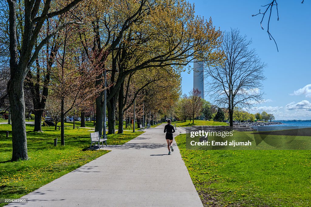 Runner on waterfront path in park with tall tower in background
